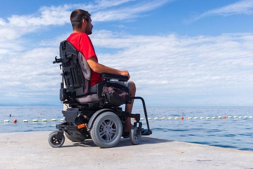 This image shows a young man in a wheelchair looking at the ocean.