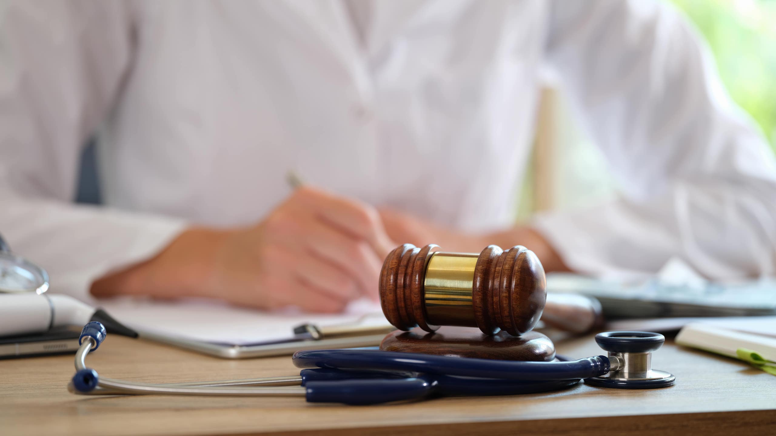 Lawyer Writing On A Paper With Gavel and Stethoscope in Front