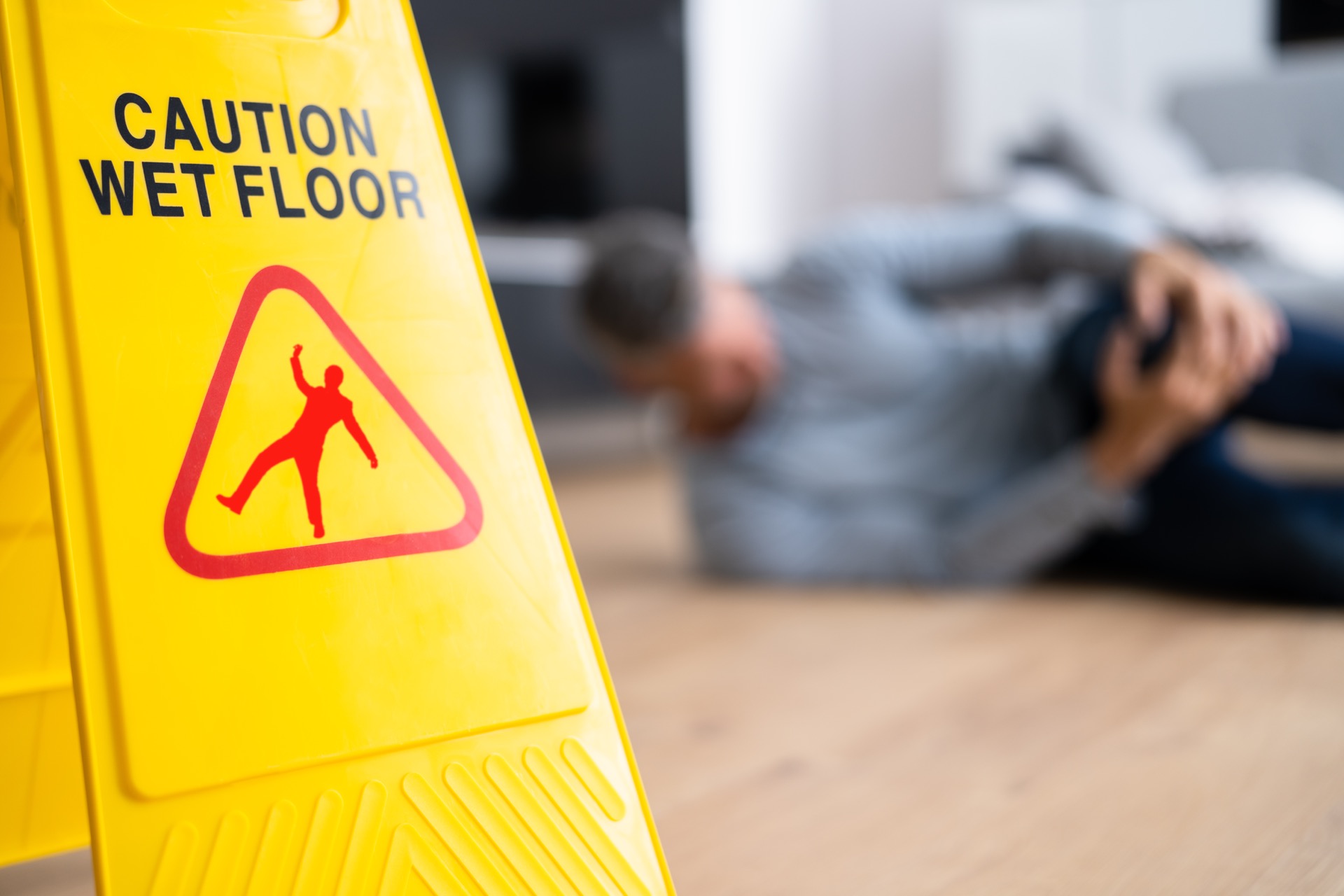 Caution Wet Floor Sign and a Person Holding His Knee on the Background