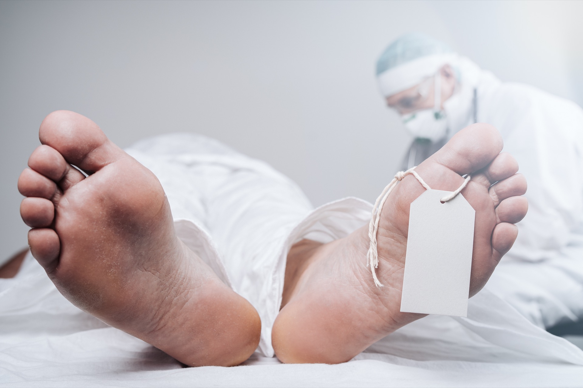 Feet of a Dead Person While the Doctor Performs the Autopsy on the Background