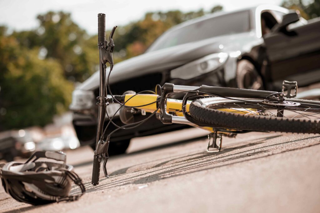 Damaged bicycle lying on road after accident with black car, representing cyclist crash scene. Damaged bicycle lying on road after accident with black car, representing cyclist crash scene.