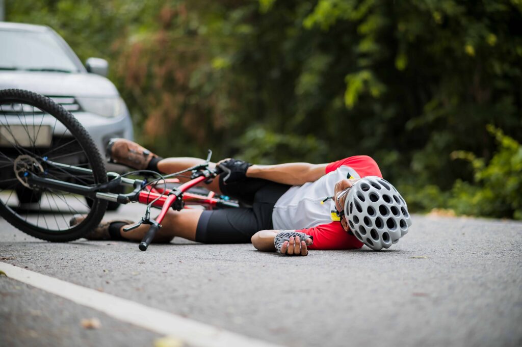 Cyclist wearing helmet injured on road after bicycle accident involving a car. Cyclist wearing helmet injured on road after bicycle accident involving a car.