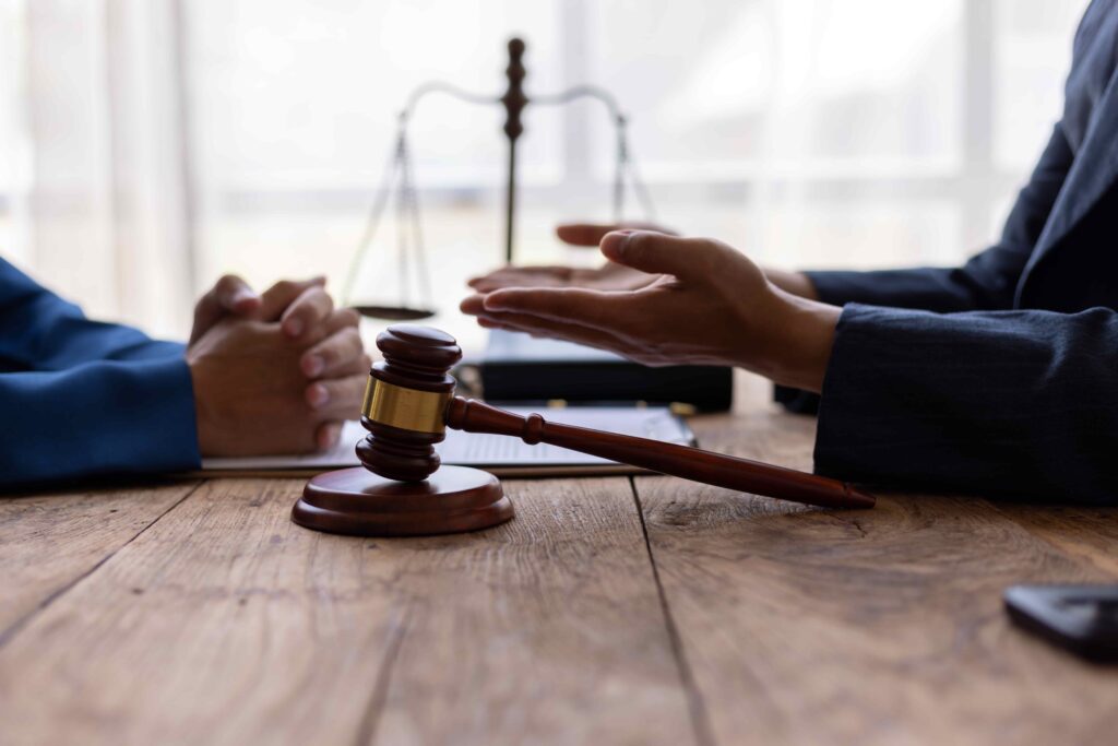 Lawyer consulting with client in office with gavel and justice scales on wooden desk.