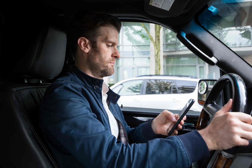 Driver using a smartphone while behind the wheel, distracted driving and texting while driving safety risk.