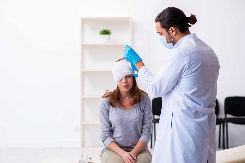Doctor treating a woman’s head injury with bandages in a medical clinic after an accident.