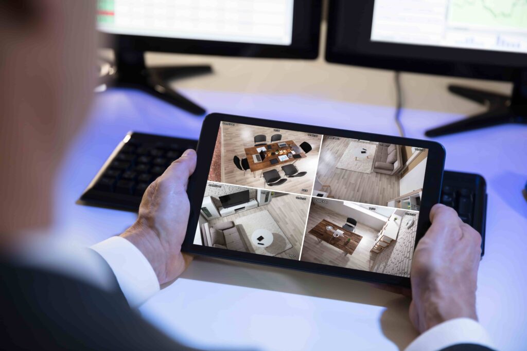 Person monitoring home security cameras on a tablet displaying multiple CCTV feeds, representing remote surveillance and security system monitoring.