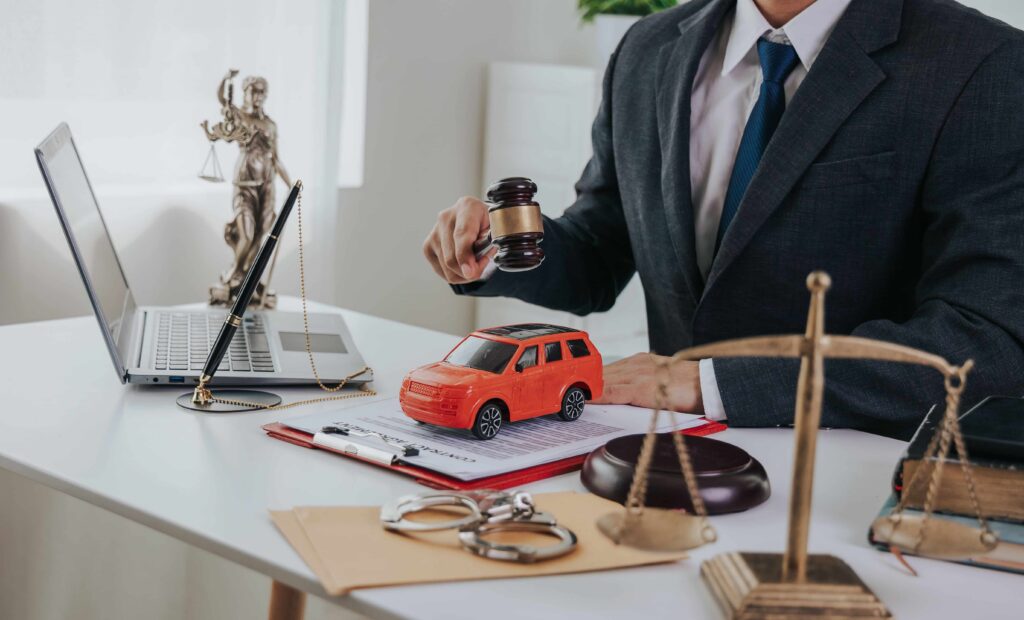 Car accident lawyer reviewing a motor vehicle case with a toy car, judge&rsquo;s gavel, and legal documents on a desk, representing auto accident legal claims.