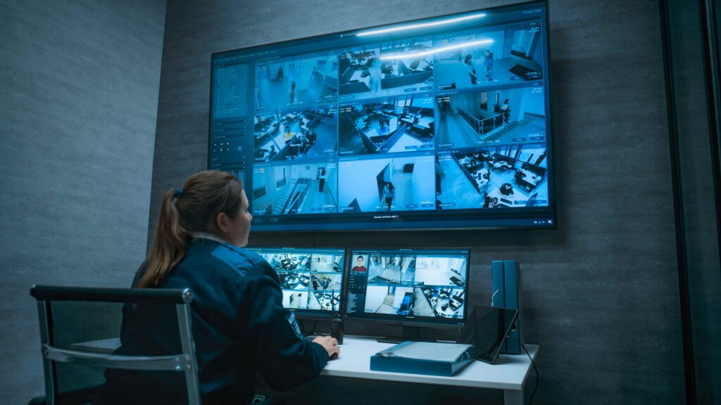 Security officer monitoring multiple surveillance cameras on screens in a security control room, overseeing CCTV footage for safety and incident investigation.